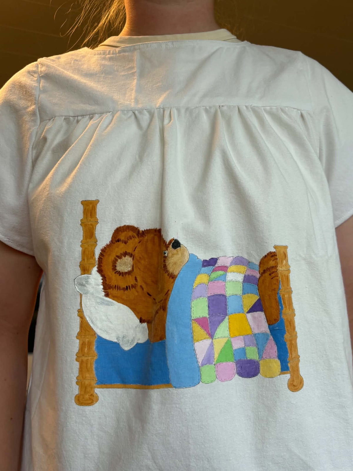 Close-up of sleeping teddy-bear appliqué on white top